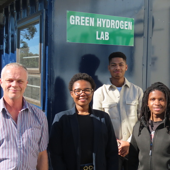 A group of people standing in front of a blue containerDescription automatically generated